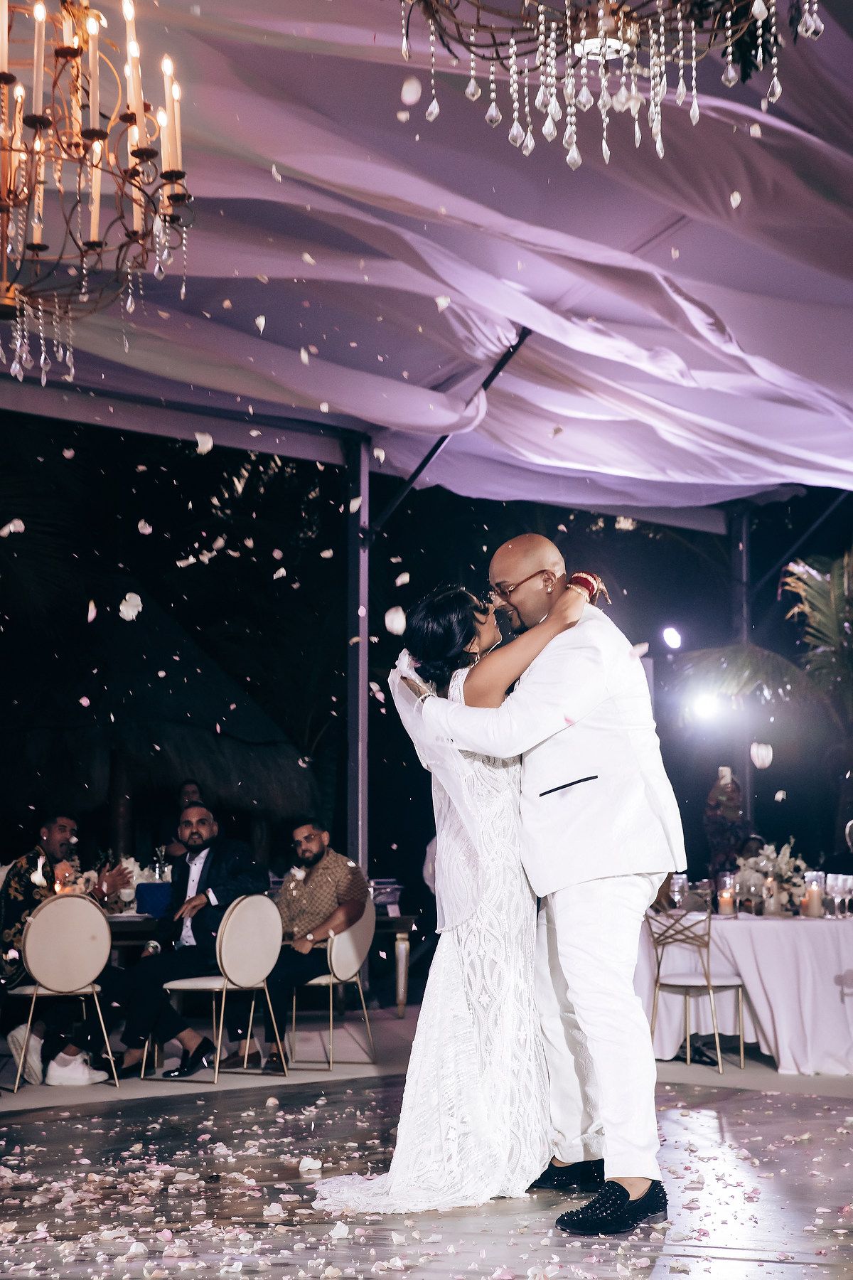 Romantic wedding dance moment under elegant crystal chandeliers with confetti falling.