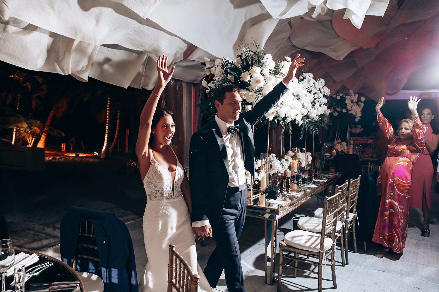 Wedding celebration with hands raised in joy under dramatic white ceiling draping.