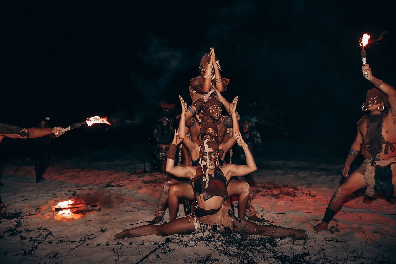 Fire dancers create dynamic patterns with burning torches during a beachside performance under dark skies.
