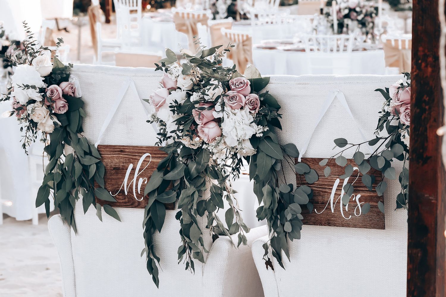 Wedding reception decor with rustic wooden signs and elegant floral greenery garlands.