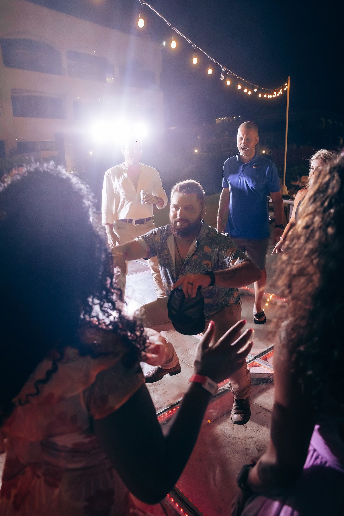 Nighttime wedding party dancing and celebrating under outdoor string lighting.
