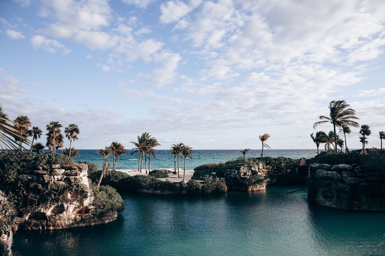 Panoramic view of a tropical oceanfront wedding venue with palm trees and rock formations.