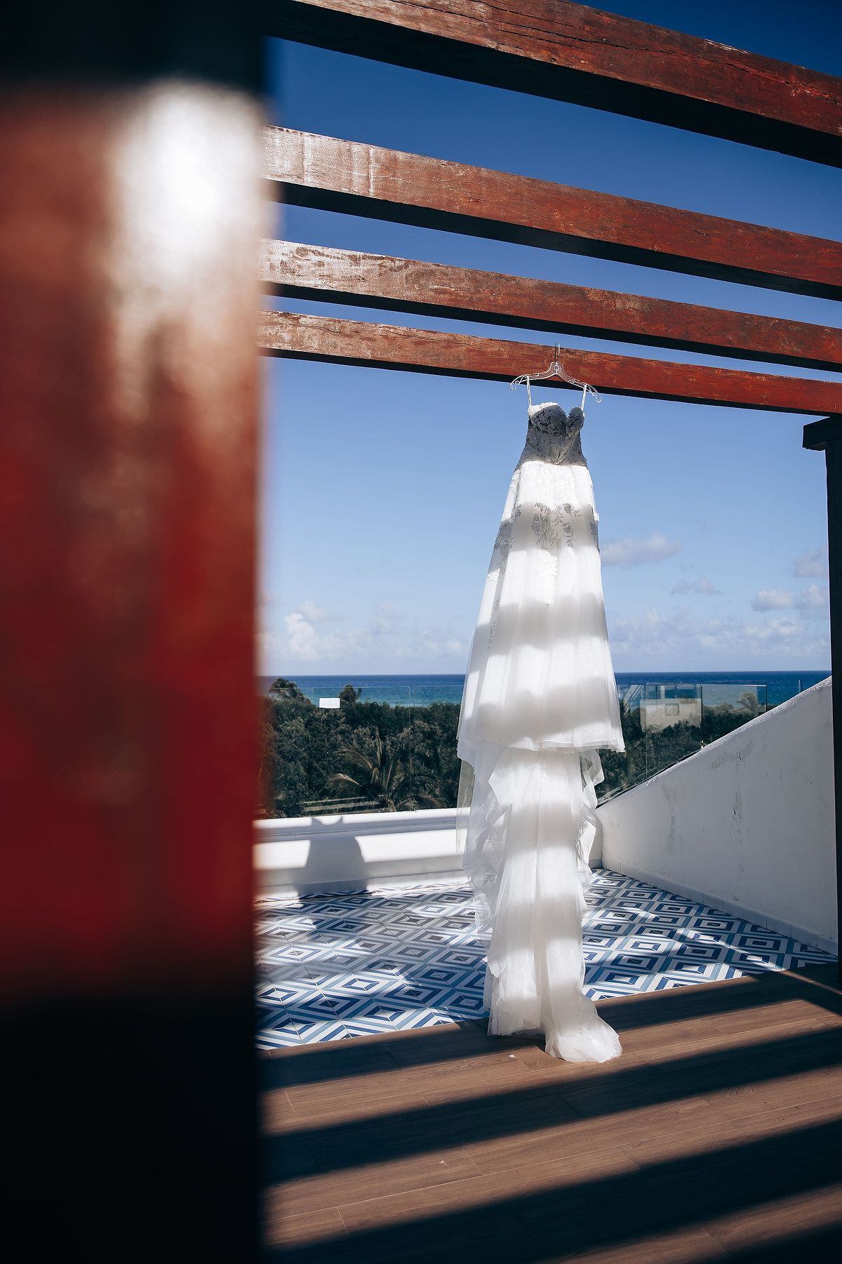 White wedding dress hanging by wooden beams against blue sky and ocean view.