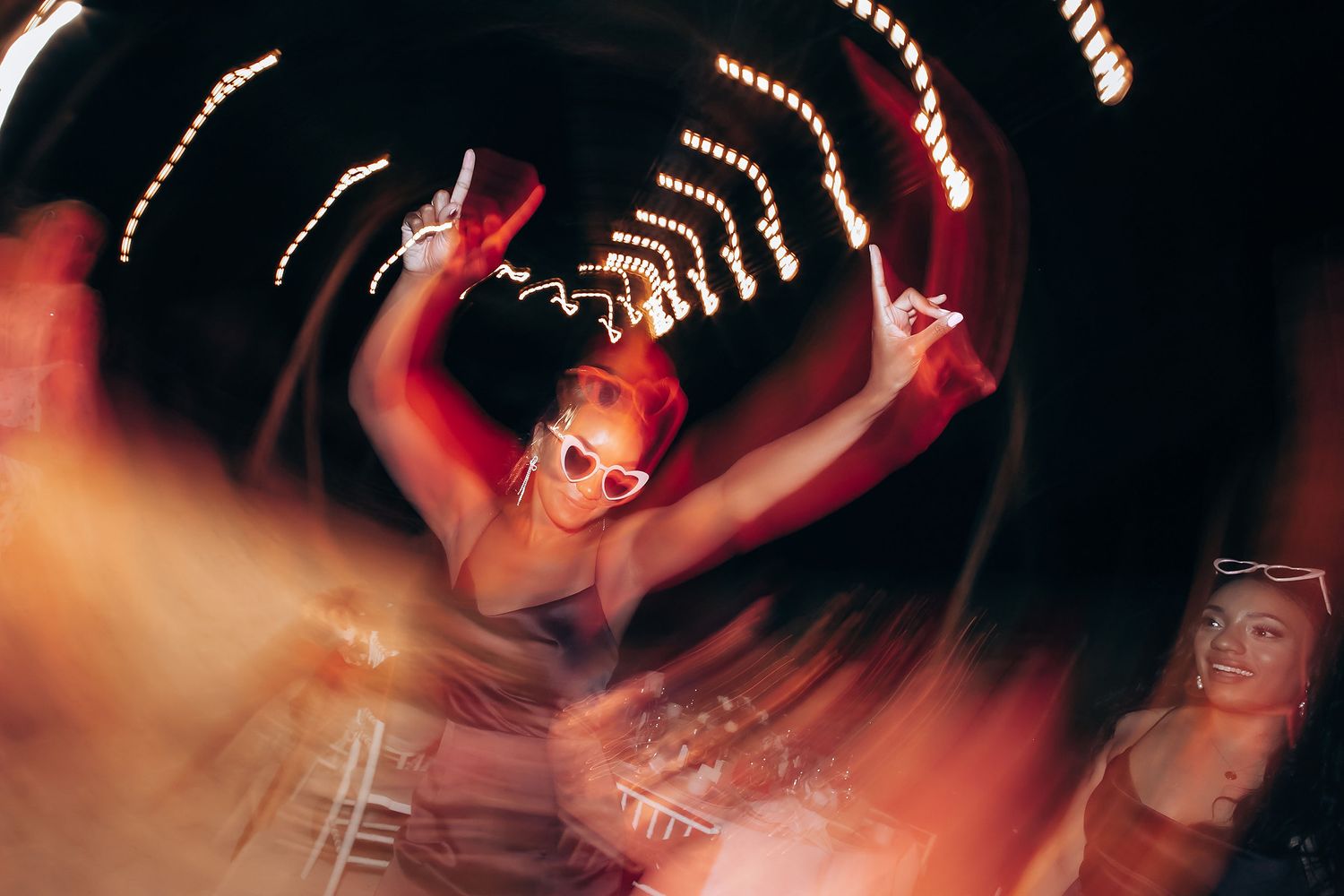 Wedding guests dancing energetically on a dimly lit dance floor with string lights overhead.