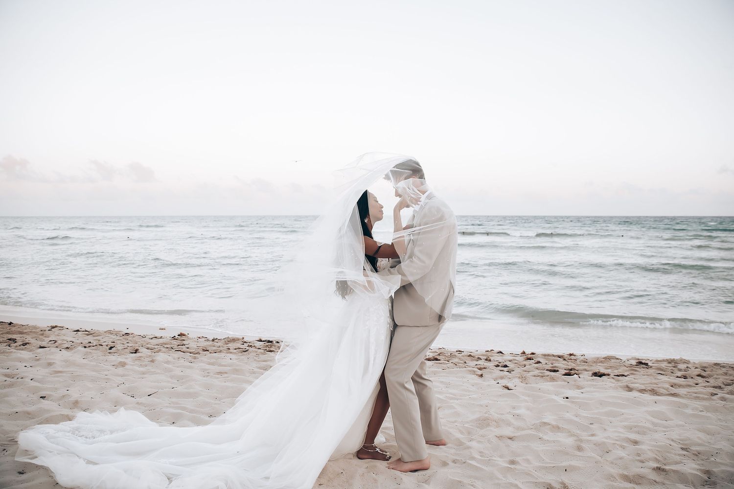 Couple taking romantic photos on a white sandy beach at sunset.
