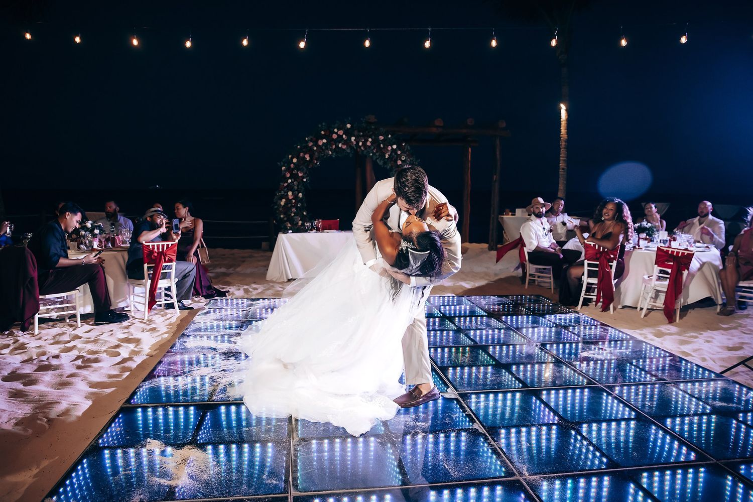 Nighttime wedding reception by illuminated pool with string lights creating romantic ambiance.