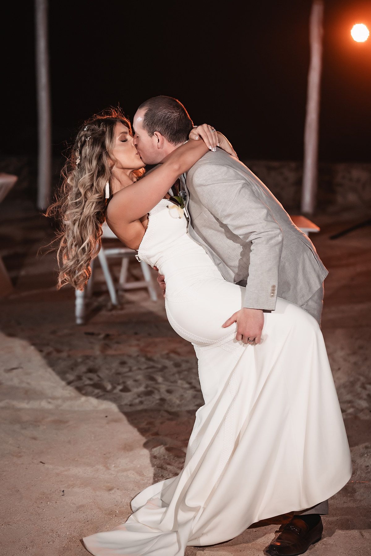A romantic dip kiss between newlyweds during their evening beach wedding celebration.