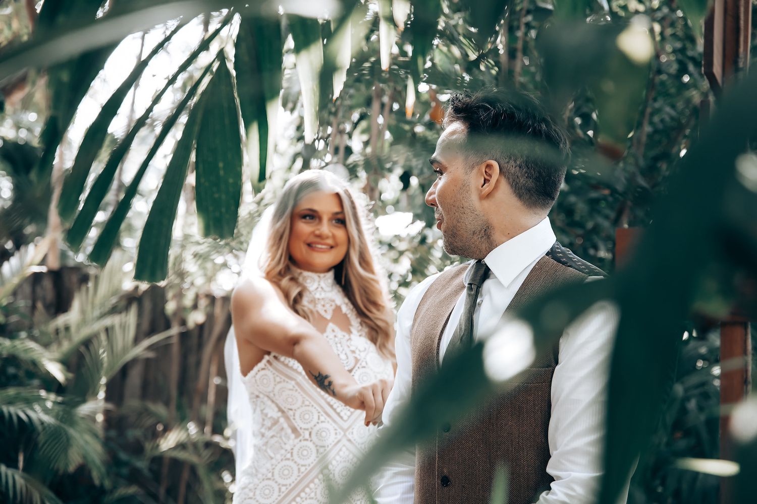 Couple sharing tender moments among tropical foliage and dappled sunlight.