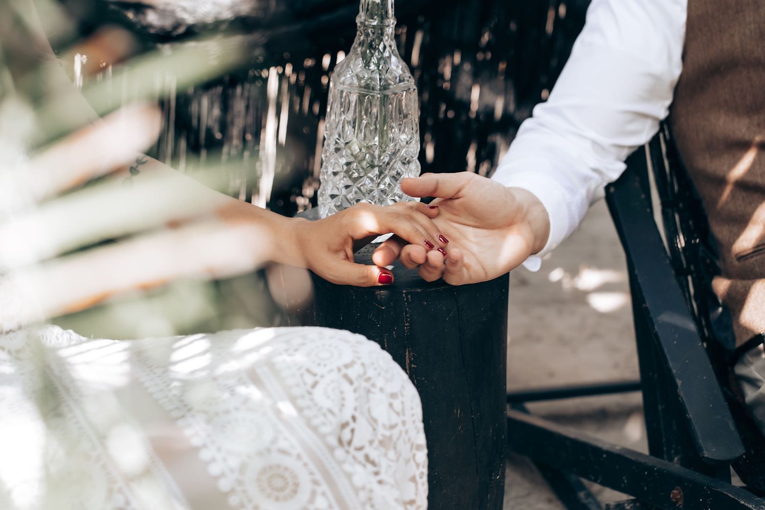 Close-up shot of hands exchanging wedding rings during an outdoor ceremony with sunlight filtering through trees.