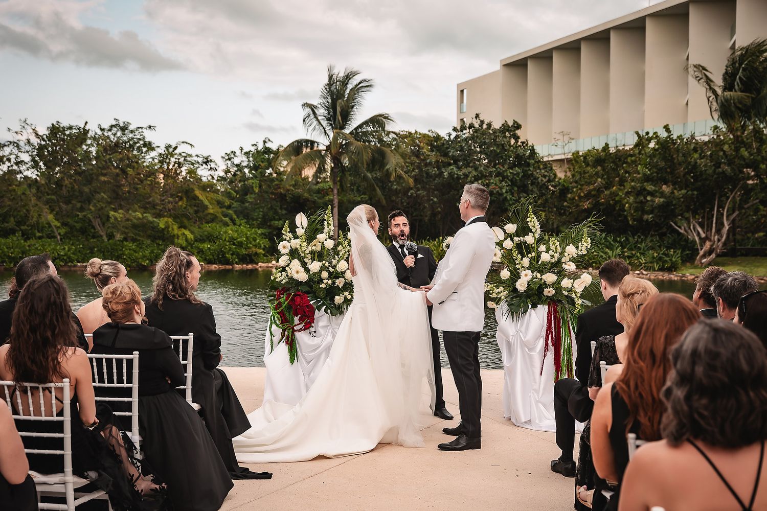 Wedding ceremony in progress at an elegant outdoor venue with tropical landscaping.
