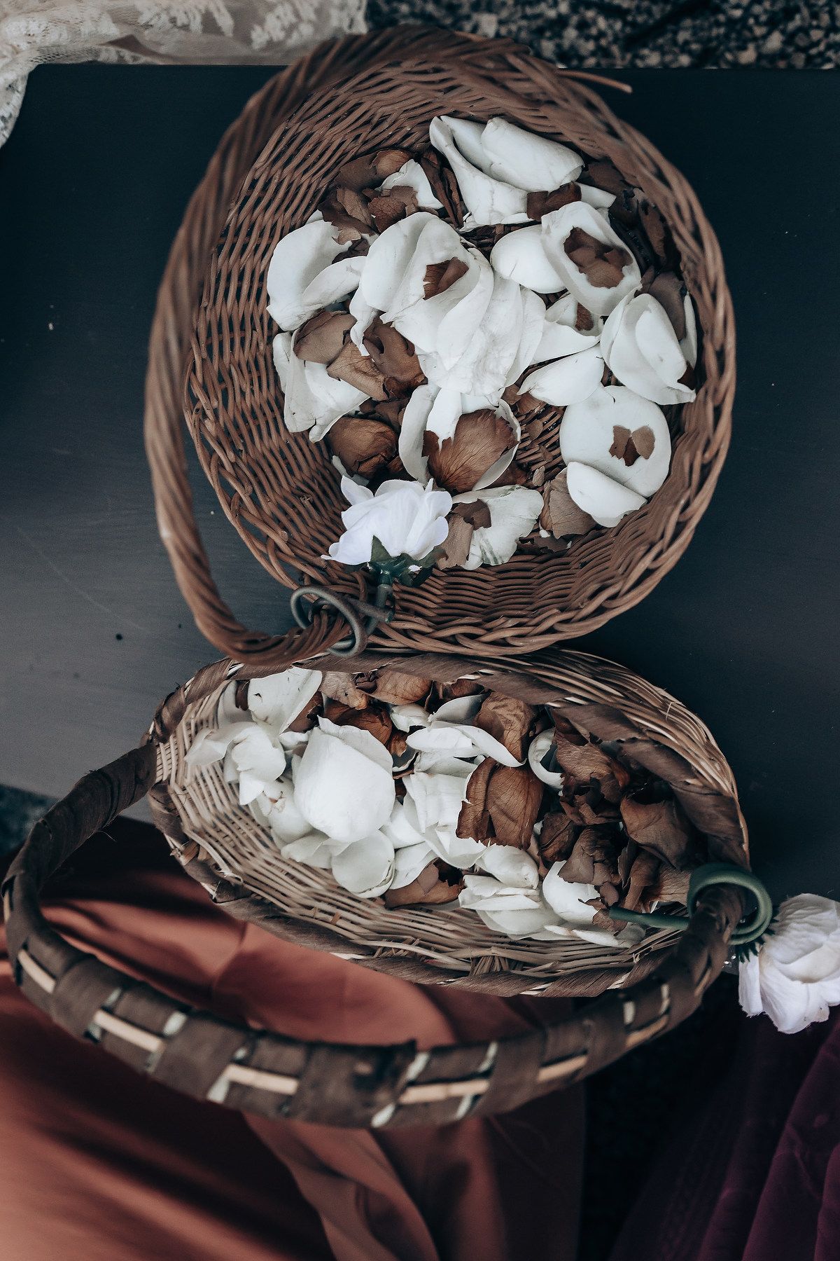 Brown wicker basket filled with white and chocolate colored flower petals for a wedding ceremony.
