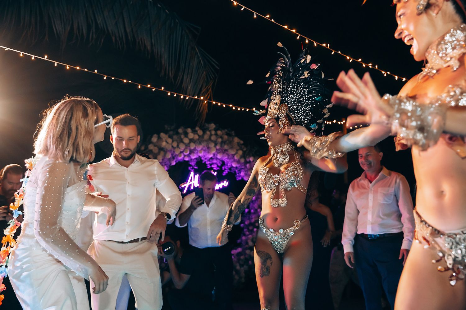 Wedding guests dancing and celebrating under string lights at night reception.