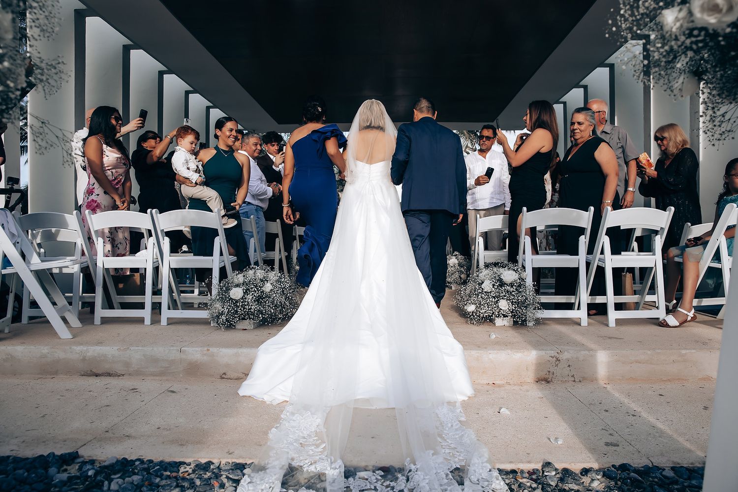 Wedding ceremony setup with white chairs and floral decorations under covered walkway.