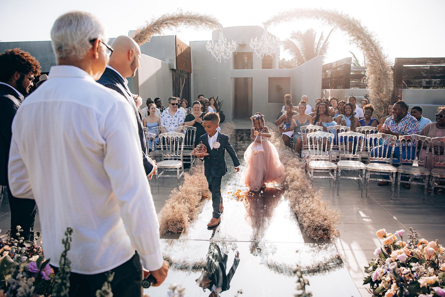 A couple walks down the aisle at an outdoor wedding ceremony while guests throw glitter creating a magical effect in sunlight.