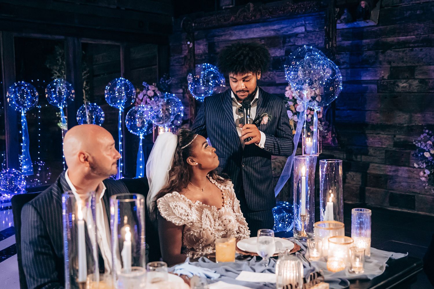 Guests celebrating at an elegant wedding reception with glowing candles and blue lighting decorations.