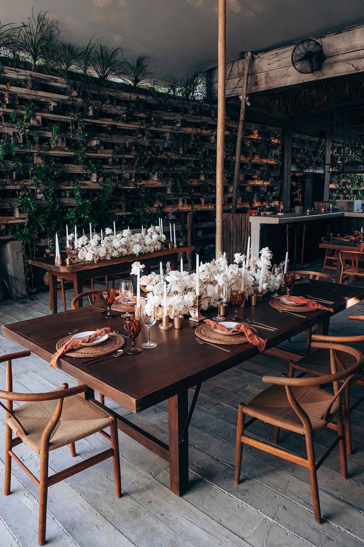 Elegant table setting with white candles and wooden chairs in a rustic indoor-outdoor dining space.