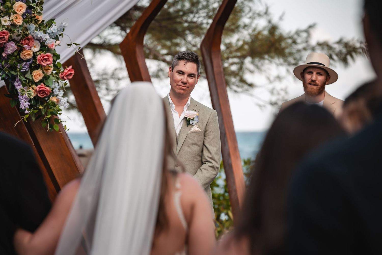 Intimate beach wedding ceremony under a modern wooden arch with floral decorations.