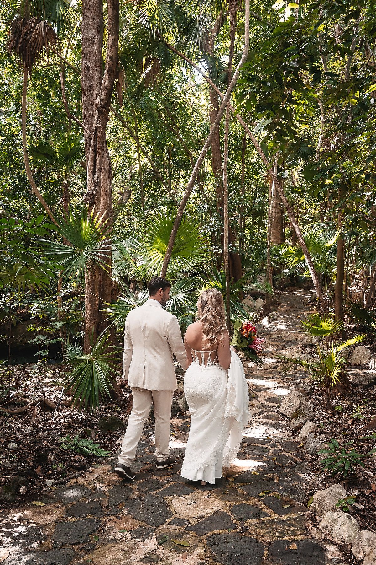 Couple walking hand in hand through a scenic tropical forest pathway.