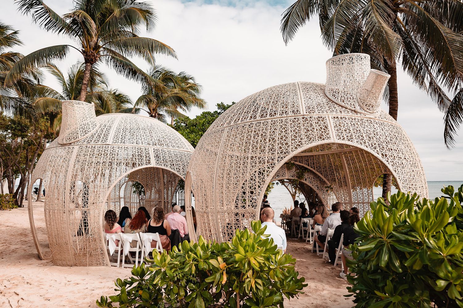 White dome structures create elegant beachside wedding venue with palm trees swaying overhead.