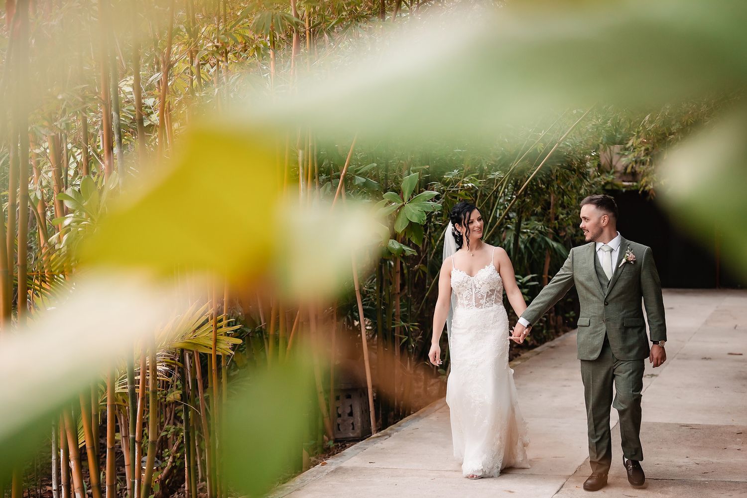 Couple strolling along a garden pathway framed by bamboo and tropical foliage.