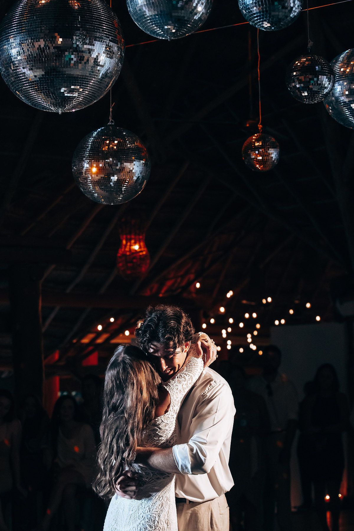 Couple dancing beneath sparkling disco balls at an evening wedding reception.