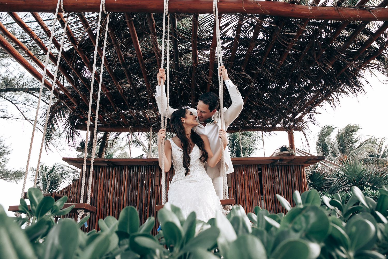 Tropical outdoor wedding ceremony setup with hanging floral arrangements and wooden beams.