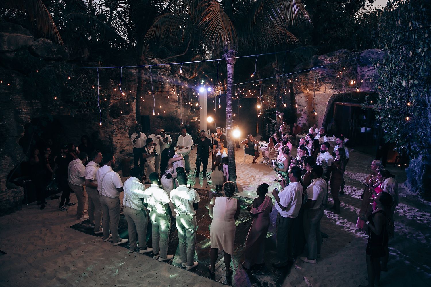 Wedding reception guests dance and celebrate under twinkling lights at an outdoor evening celebration.