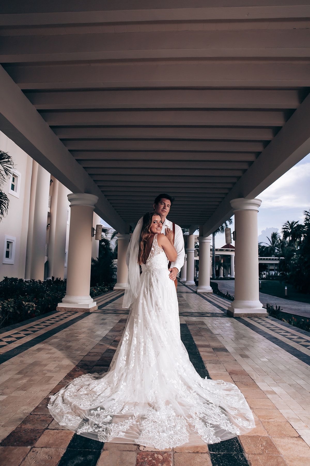 Stunning bridal portraits under a columned walkway showcasing a long lace train and architectural details.