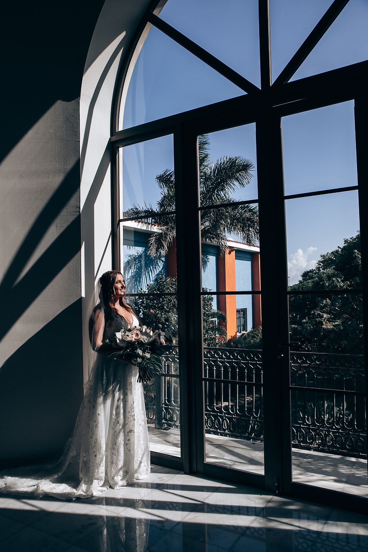 Dramatic shadows cast through large windows in an architectural space with palm trees visible outside.