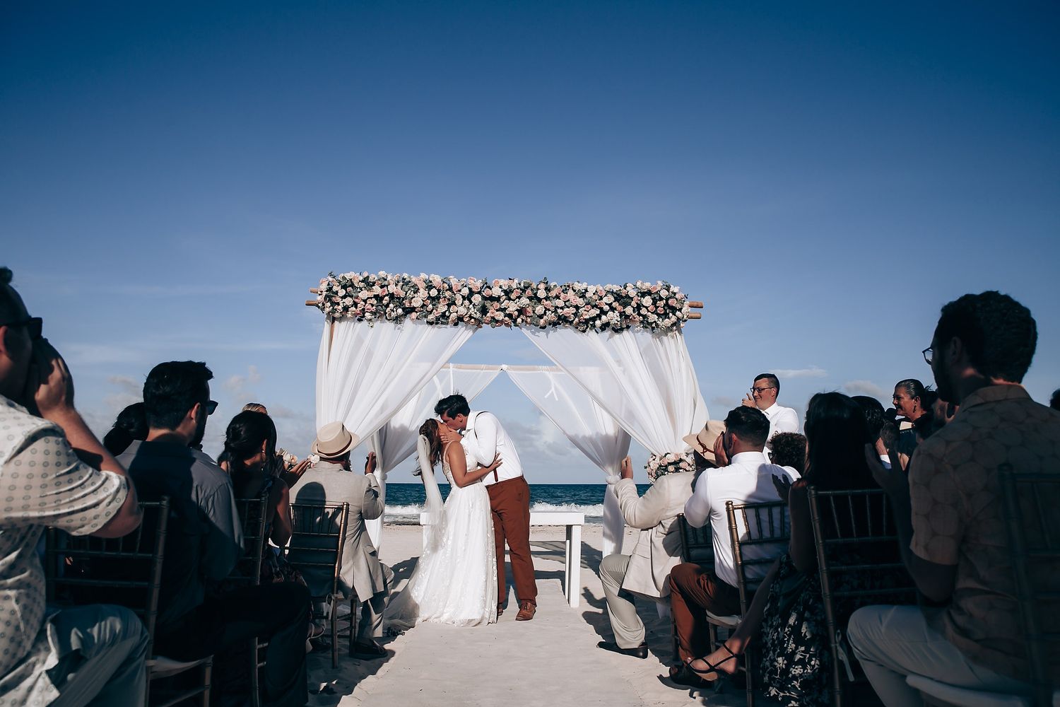 Outdoor wedding ceremony setup with white chairs against a bright blue sky backdrop.