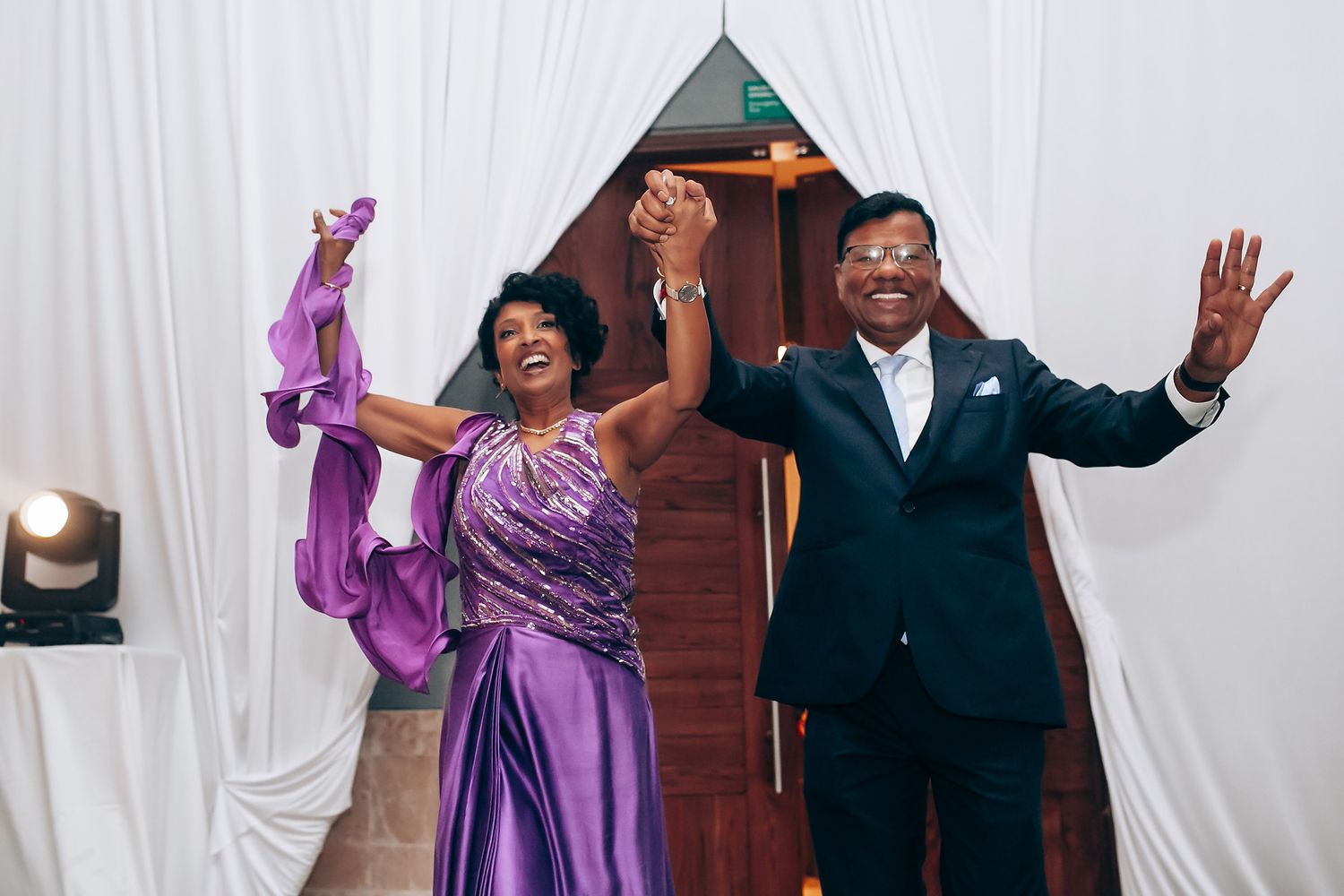 Couple celebrating in formal attire, with one wearing a purple gown and the other in a navy suit.