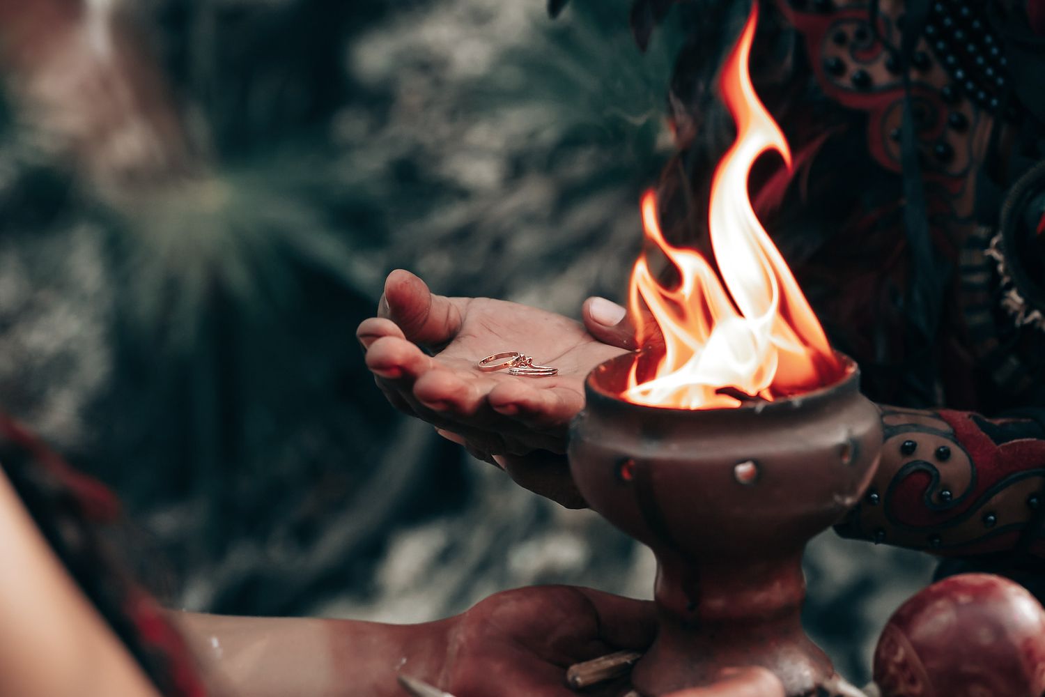 A hand holds a burning incense stick in a natural, outdoor setting.