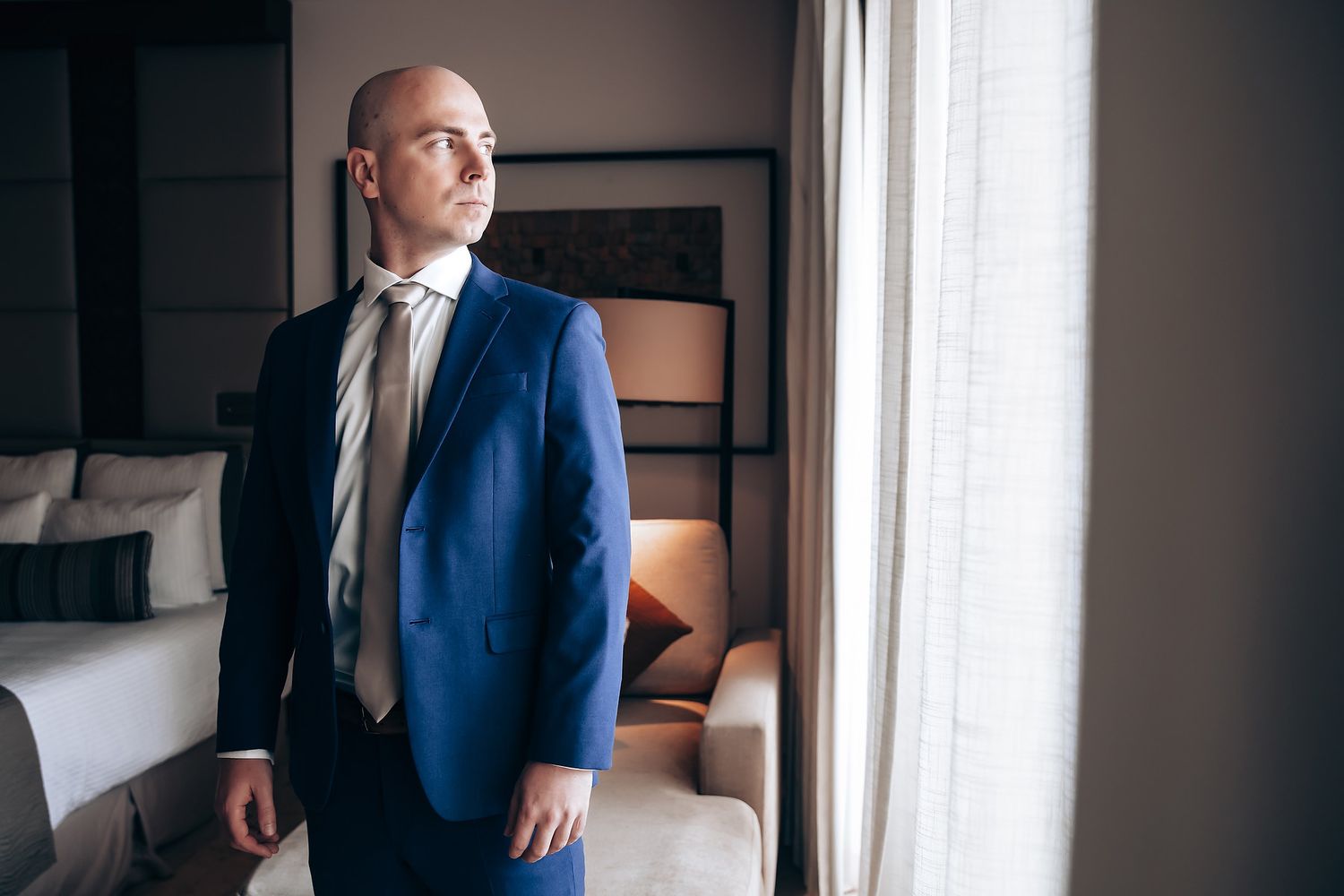 A businessman standing by a window in what appears to be an office or hotel room.