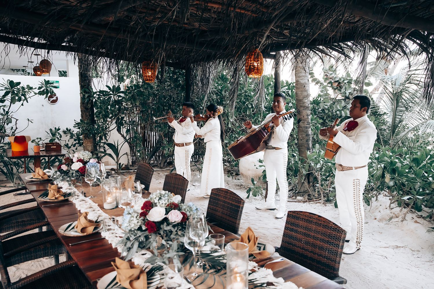 A group of people enjoying a meal outdoors in a tropical setting with thatched roof structures.