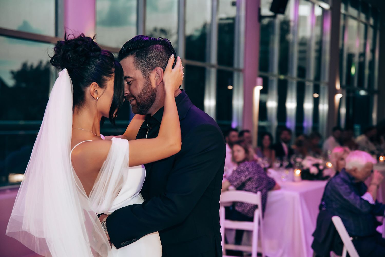Wedding couple dances together under purple mood lighting during their reception celebration.
