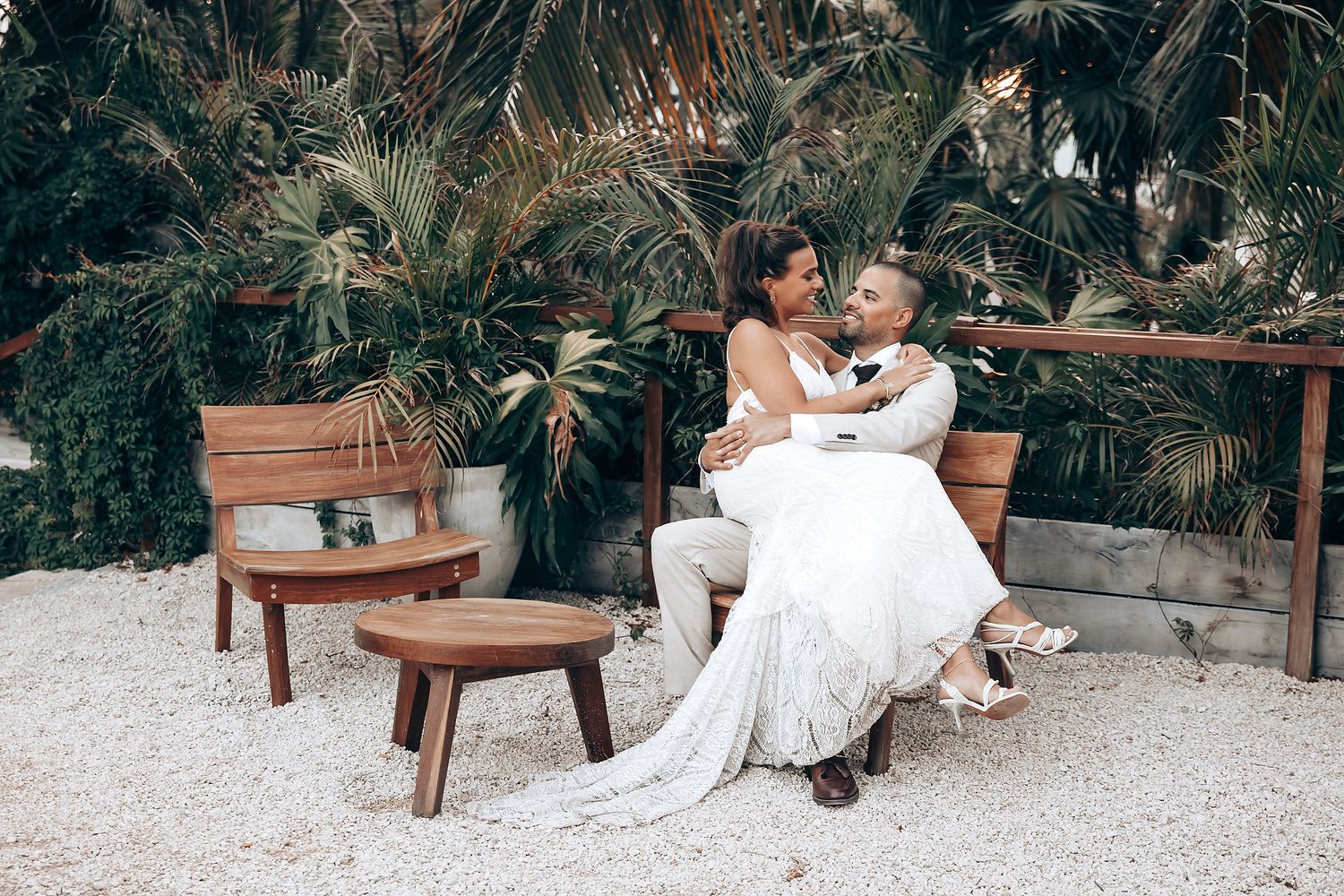 Elegant wedding scene with wooden benches and tropical greenery in a beachside setting.