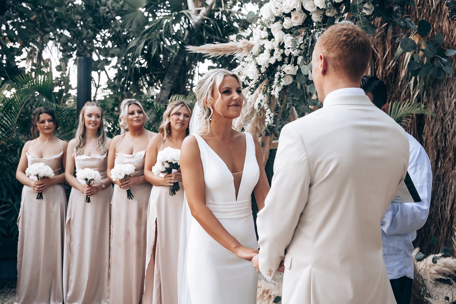 Bridesmaids in neutral dresses standing together during outdoor ceremony.