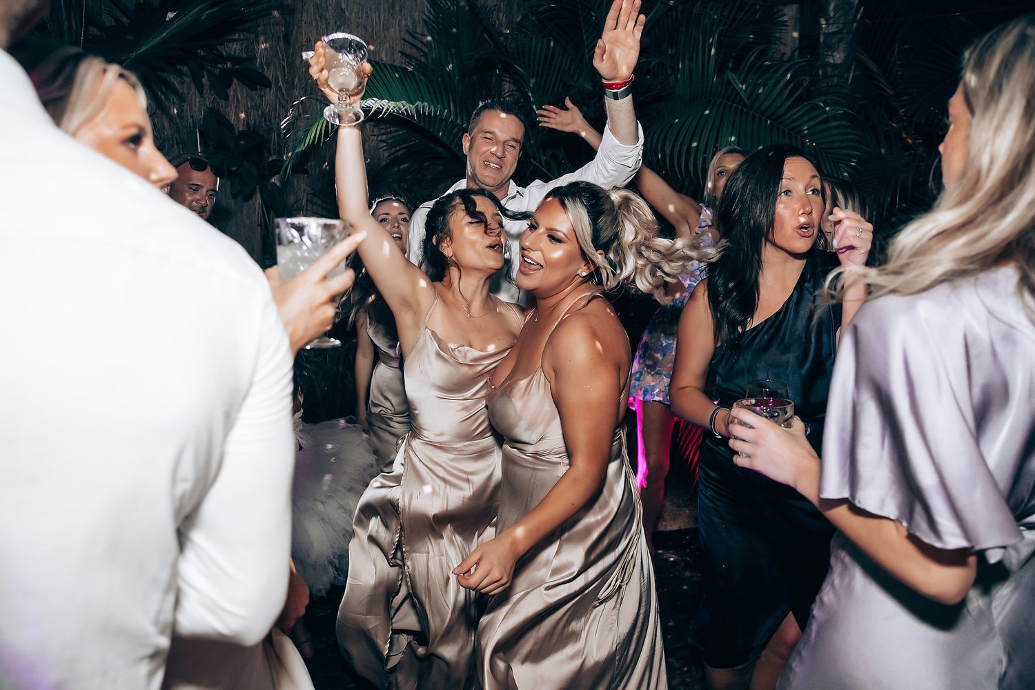 People dancing and celebrating with raised hands in a dark nightclub atmosphere.
