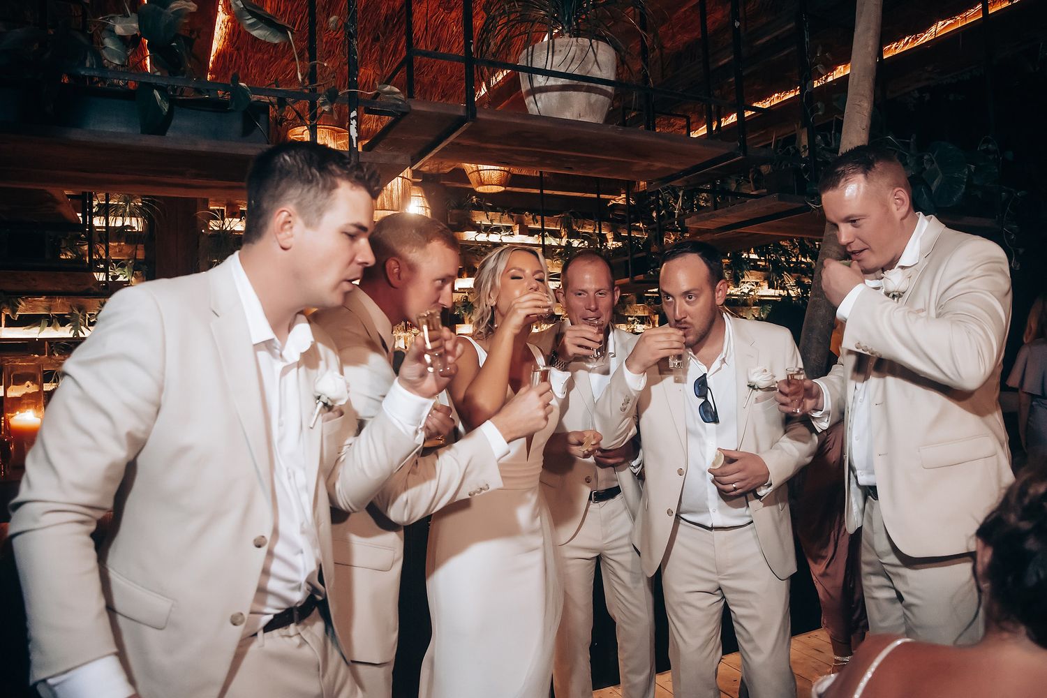 Wedding guests in white attire celebrate on the dance floor at an indoor reception.