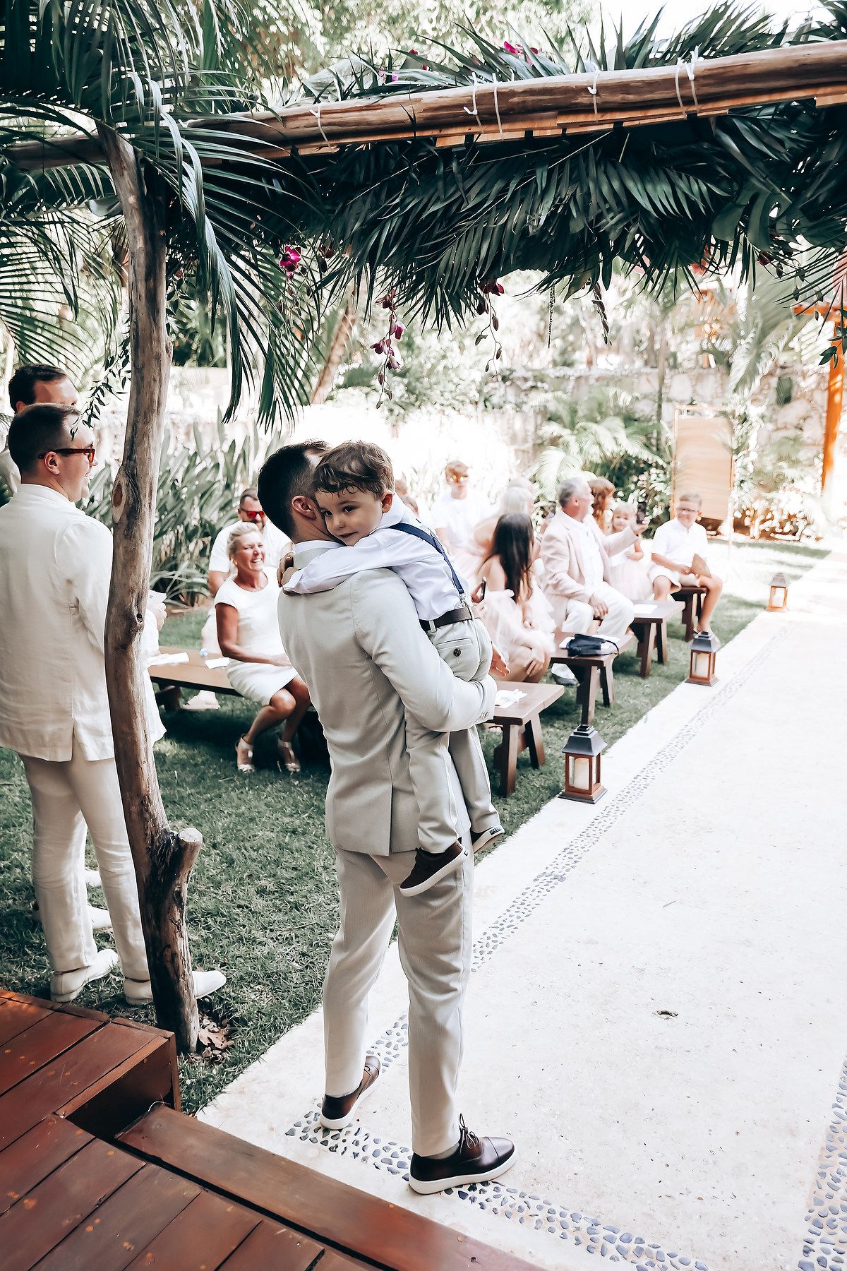 Wedding reception dance floor under palm trees with guests in light-colored attire.