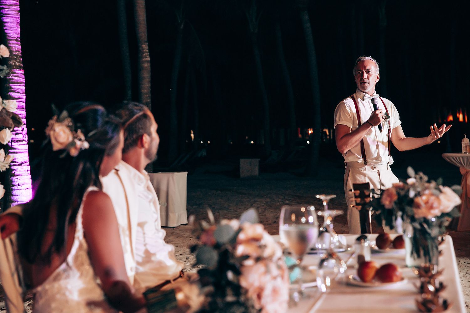 Purple uplighting creates ambiance at a nighttime wedding reception as guests dance.