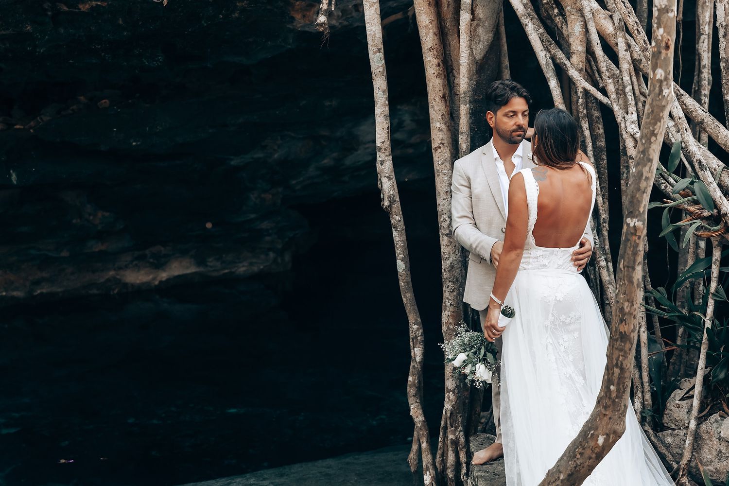 A wedding ceremony unfolds among tropical trees and natural stone formations.