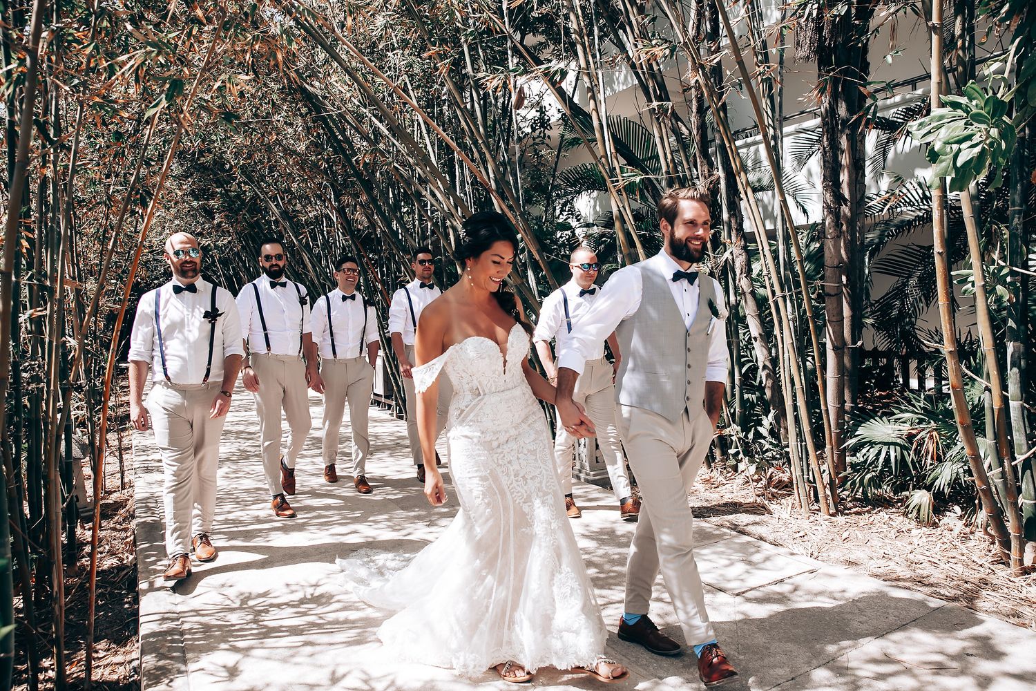 Wedding celebration in a natural wooded setting with white-dressed attendees walking along a path.
