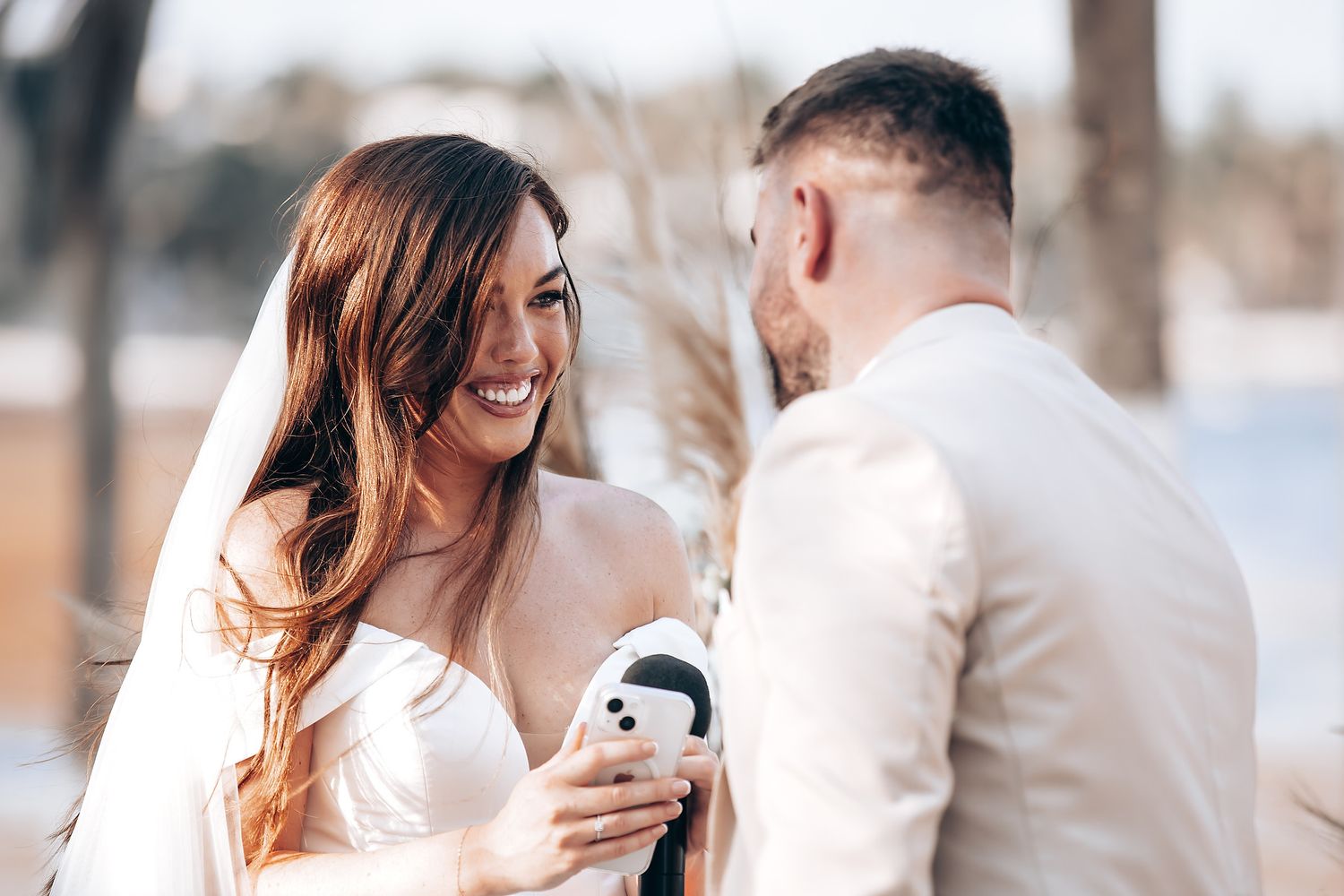 A couple in formal wedding attire shares an intimate moment during a photoshoot by a waterfront.