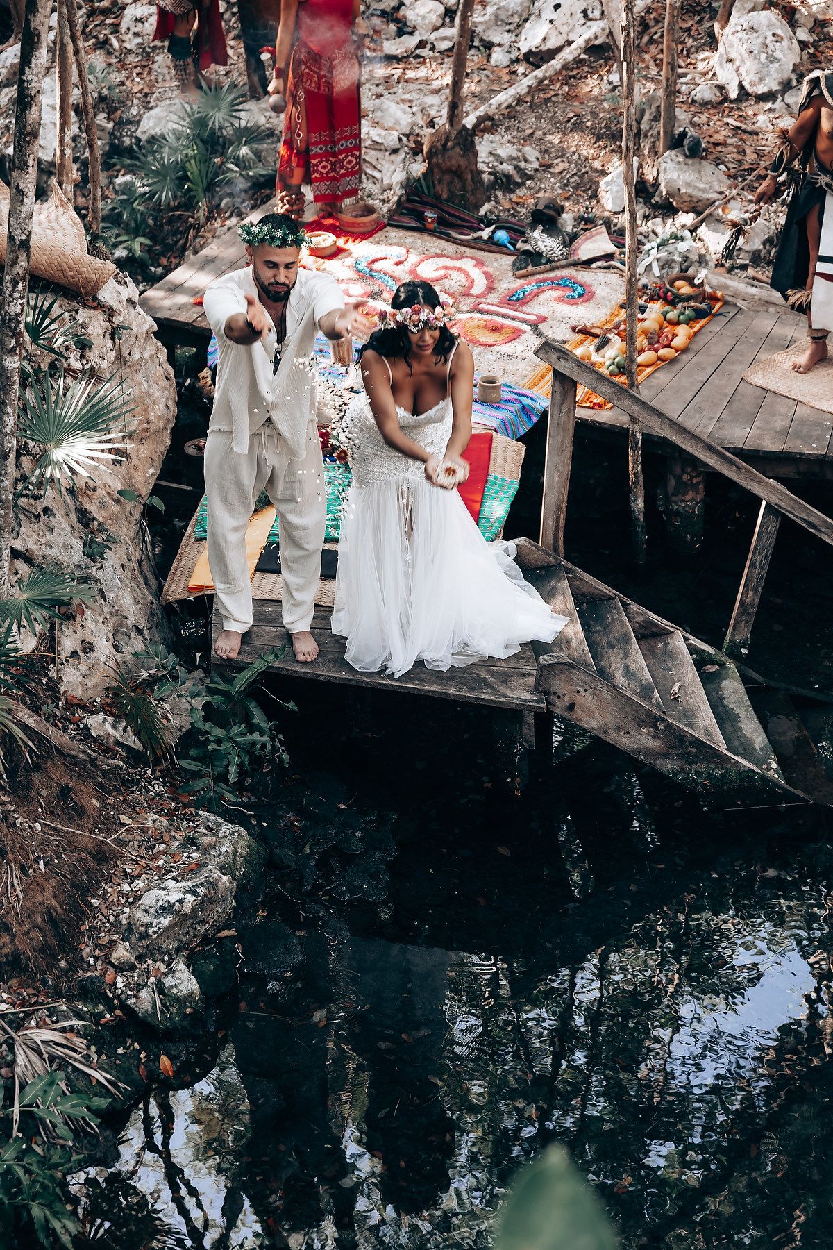 A rustic outdoor wedding ceremony setup near a natural cenote or water feature in a wooded area.