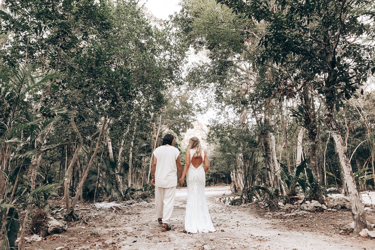 A couple walks hand in hand down a tree-lined path in a romantic outdoor setting.