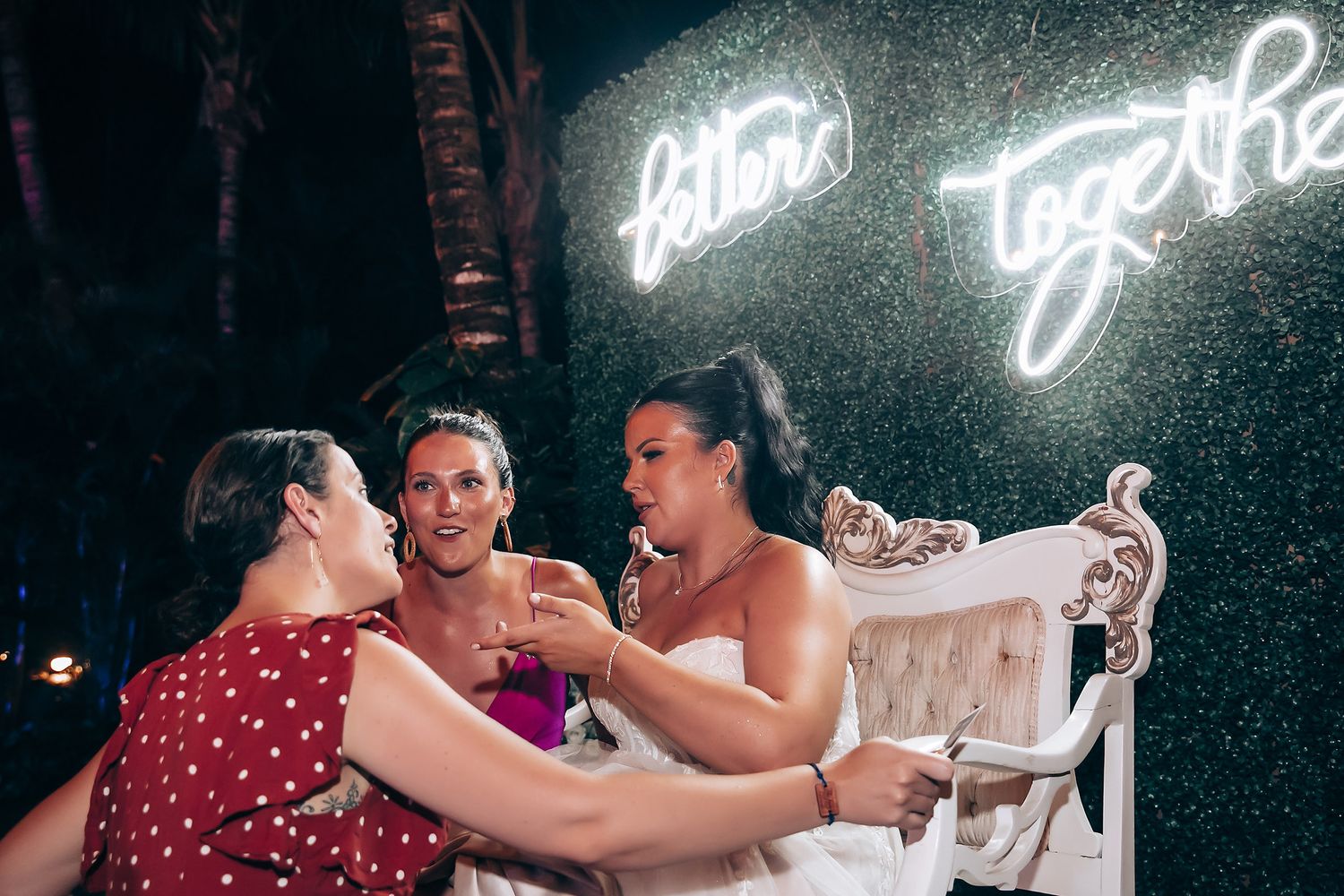 Wedding party celebrates on dance floor under neon lights and glowing signage.