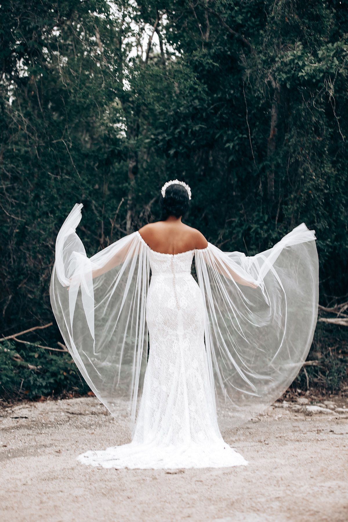 A figure in a flowing white dress with billowing sleeves poses dramatically against a wooded outdoor setting.