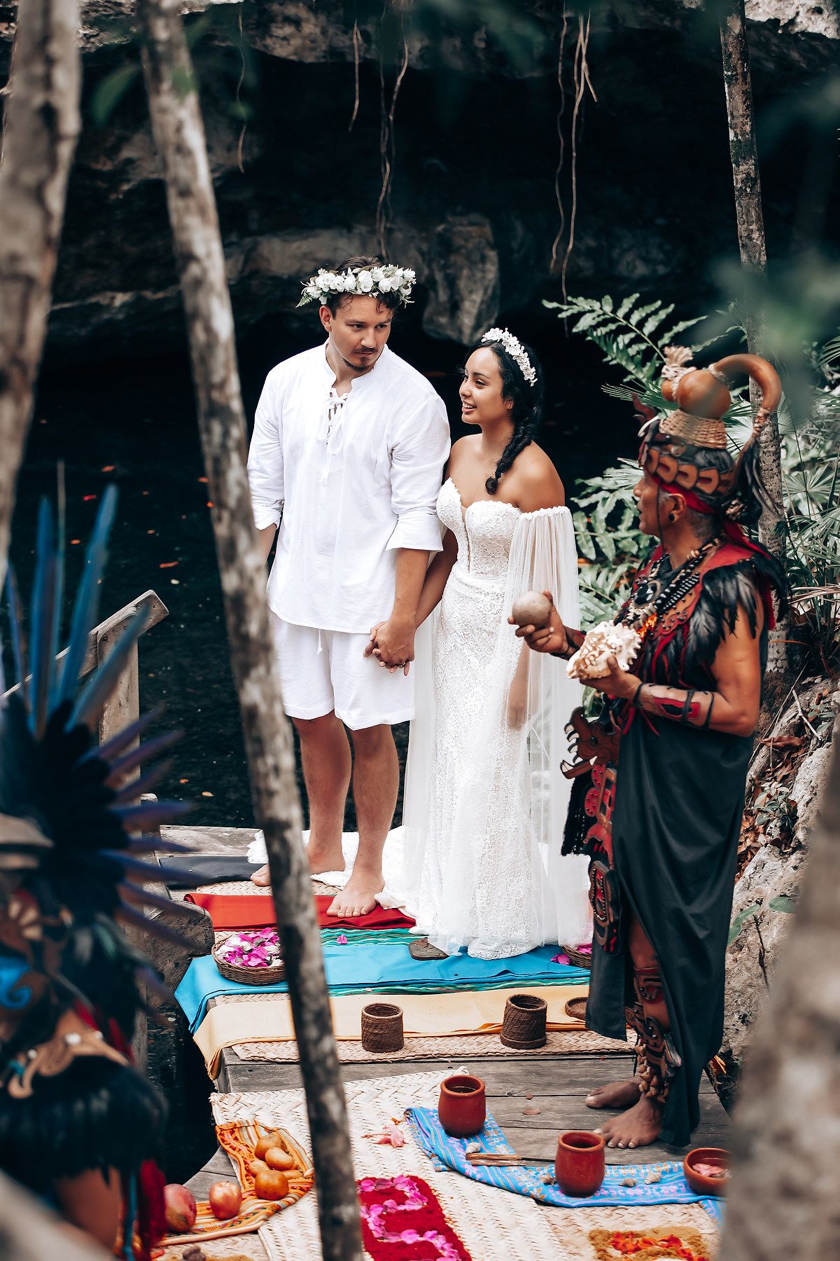 Traditional Hawaiian wedding ceremony takes place outdoors with a spiritual officiant and tropical foliage in background.