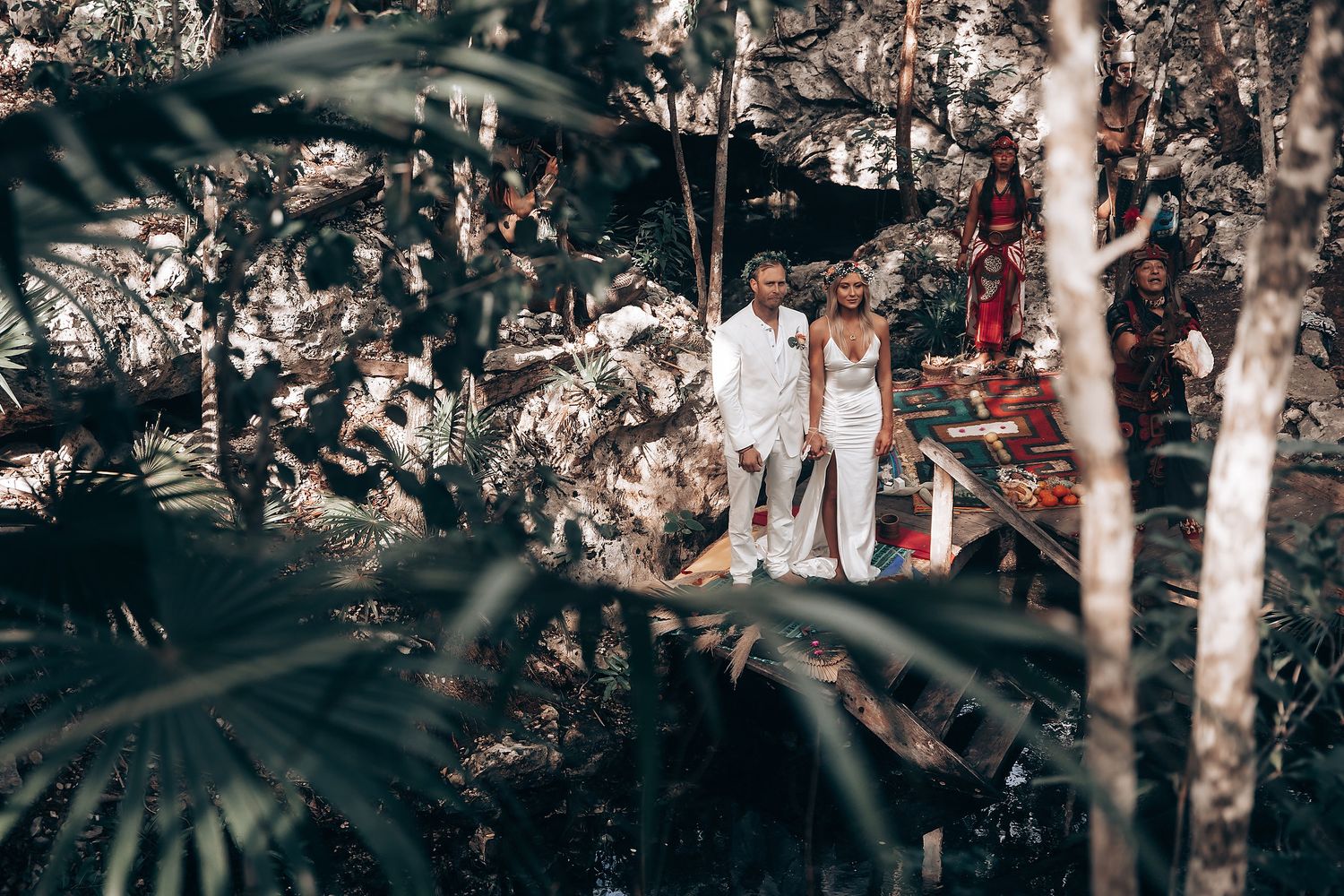 People in white clothing standing among tropical foliage during a Mayan ceremony.